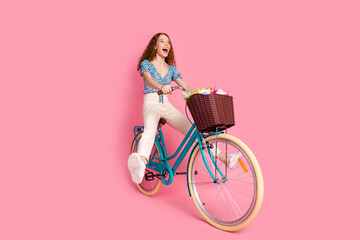 Happy young woman riding bicycle on pink background