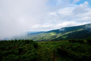 A scenic view of a lush green valley surrounded by forested hills under a partly cloudy sky.