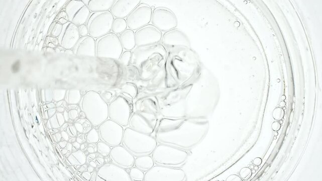 Transparent air Bubbles come out from lab pipet and bursting on the surface of clear fluid in Petri dish. The medicine concept, health care, treatment. Macro Shot of Natural Organic Cosmetics. 4k