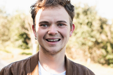 Smiling transgender man in a casual setting surrounded by greenery during daytime