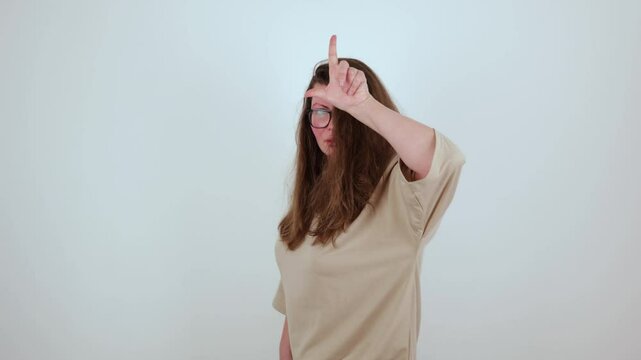 Plus size woman in beige t-shirt against white wall, making an L sign loser on her forehead, symbolizing self-empowerment through embracing imperfections and redefining failure.