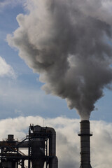 Naklejka premium Chimney of a wood processing plant. Chimney with white smoke in a blue sky with white clouds