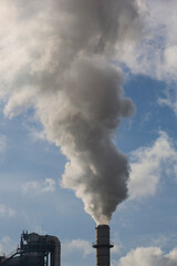 Chimney of a wood processing plant. Chimney with white smoke in a blue sky with white clouds