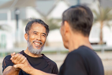 Fototapeta premium Cheerful senior Asian men sharing a handshake and laughter on a sports field, celebrating wellness and friendship.