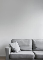 A grey sofa with a single pillow sits in front of a white wall