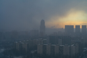 Fototapeta premium A snowstorm covers the big city, a gloomy sky with glimpses of the sun. Aerial shooting. Space for text.