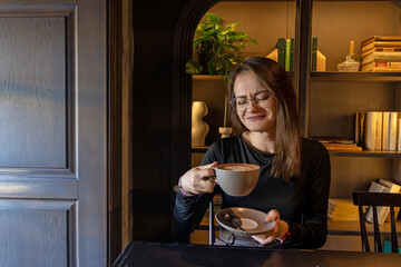 Woman wincing while tasting coffee. A woman in glasses winces slightly after tasting a cup of coffee at a cafe, seated near a bookshelf in warm lighting.