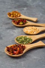 Assortment of dried vegetables in small wooden spoons on a dark background. Variety of spices and herbs.