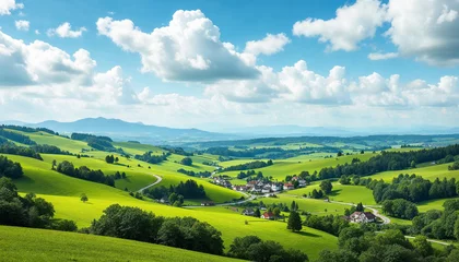Fototapeten Rolling green hills, winding road, and a quaint village under a partly cloudy sky capture rural serenity.   © abu