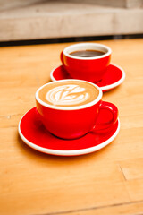 Cappuccino and Americano coffee in red cups on a wooden table