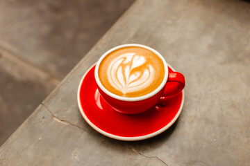 Cappuccino coffee in red cup on concrete table Delicious flat white with latte art on a gray...