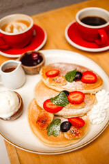Pancakes with strawberries, fried bananas, ice cream and syrup on a wooden table. Delicious breakfast with fruits, berries and coffee