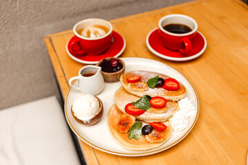 Pancakes with strawberries, fried bananas, ice cream and syrup on a wooden table. Delicious breakfast with fruits, berries and coffee