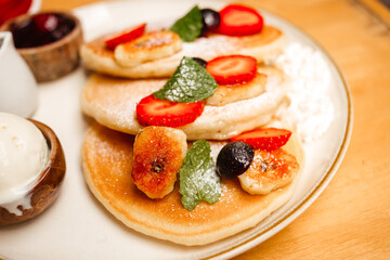 Pancakes with strawberries, fried bananas, ice cream and syrup on a wooden table. Delicious breakfast with fruits and berries