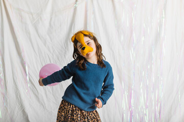Obraz premium Elementary kid plays joyfully with a pink balloon wearing a fun lion headband in a colorful indoor setting