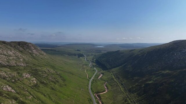 Barnesmore Gap, County Donegal, Ireland, June 2023. Drone pushes forwards in a sweeping panorama of the valley with the winding N15 road beside a meandering river and Lough Mourne in the distance.