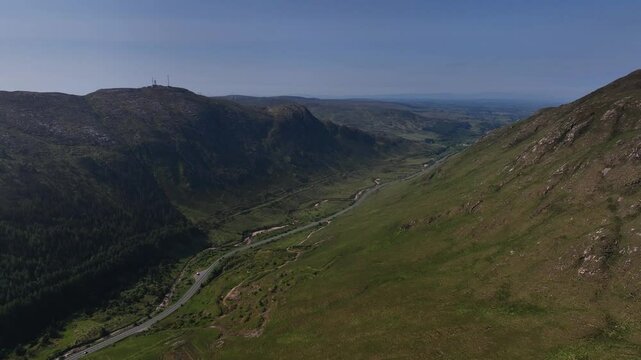 Barnesmore Gap, County Donegal, June 2023. Drone rises above mountain peaks to establish winding road through boglands connecting towns on a beautiful summer day through the lush green landscape