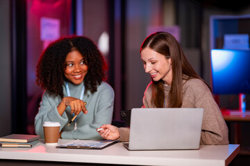 White businessman and African woman work as a team and use laptop tablet for night research. Data analysis results Comparing and planning with digital technology