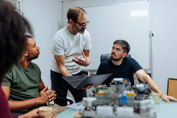 Engineers collaborating on robotics project using laptop in meeting room