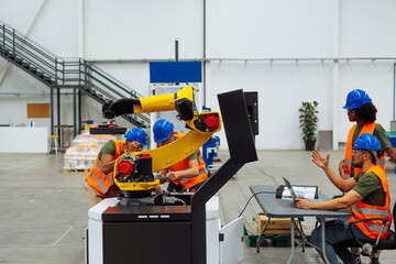 Engineers maintaining and programming robotic arm in factory