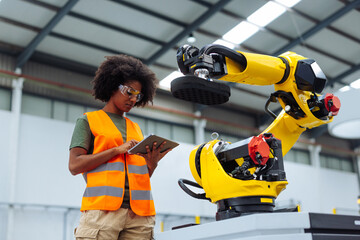 Female engineer using digital tablet while controlling robotic arm in factory