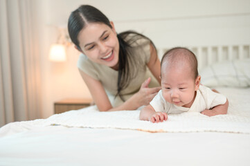 Mother Encourages Her Baby to Crawl on a Soft Bed in a Cozy Room During Afternoon Playtime