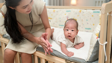 Mother Encourages Her Baby to Crawl on a Soft Bed in a Cozy Room During Afternoon Playtime
