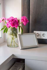 A vase with peonies next to a photo frame