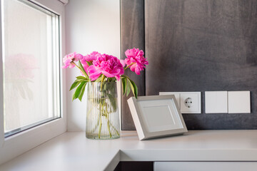 A vase with peonies next to a photo frame