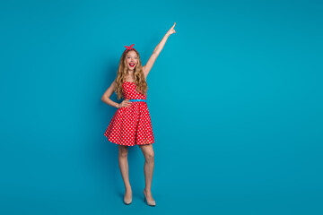 Young woman with a pinup retro style pointing upward against a bright blue background