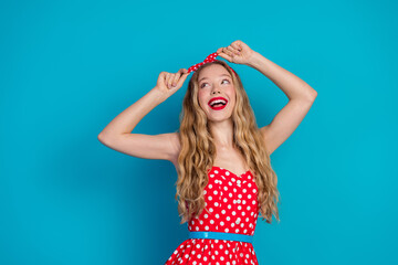 Happy young woman in retro polka dot dress with matching headband against blue background, showing...