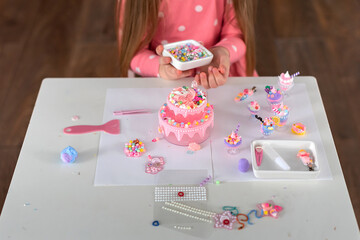 Young caucasian girl decorating miniature pink cake with colorful candy and accessories. Bead craft toy 