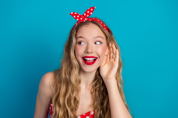 Smiling young woman with retro style and red headband sharing a secret against blue background