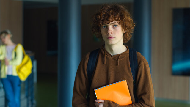 High school university teenager education study calm holding book posing in corridor alone serious Caucasian guy boy pupil teen male man schoolboy student studying learning college looking at camera