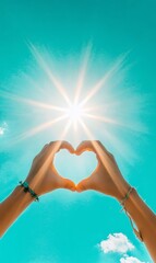 Hands forming heart shape against bright sun in turquoise sky, symbolizing love and positivity