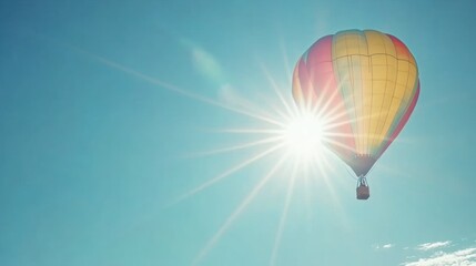 Obraz premium Colorful hot air balloon soaring in a clear blue sky, sun shining brightly behind it.