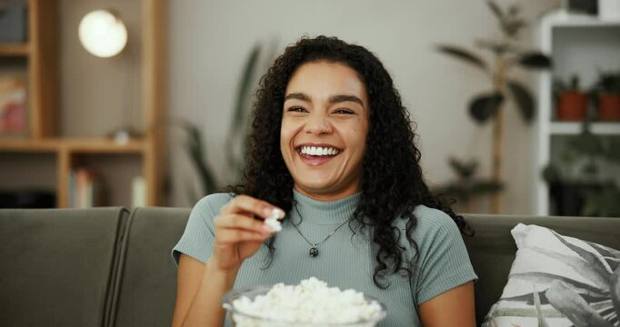 Woman, laugh or watching TV in home with popcorn, streaming service or enjoy comedy series on sofa. Girl, happy and snack in living room with funny movie, favorite sitcom and relax with entertainment