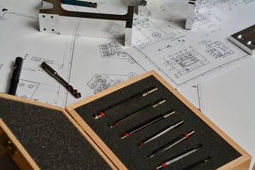 detailed photo of a workbench with technical drawings and tools. taps, drill, metal parts, blocks with drilled holes
