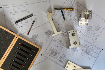detailed photo of a workbench with technical drawings and tools. taps, drill, metal parts, blocks with drilled holes