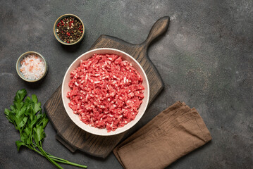 Raw mince beef with spices, ground meat in bowl on wooden cutting board, dark grunge background,...