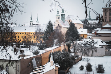 Winter cozy atmosphere in Prague with smoking chimney and church towers of Loreta and Petrin hill covered by snow evokes peaceful and quiet place during christmas in capital of Czech Republic.