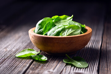 Young baby spinach leaves in a wooden plate on rustic table. Food photography