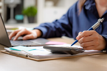 Asian woman calculating finance, money, using calculator, laptop computer at home workplace table.
