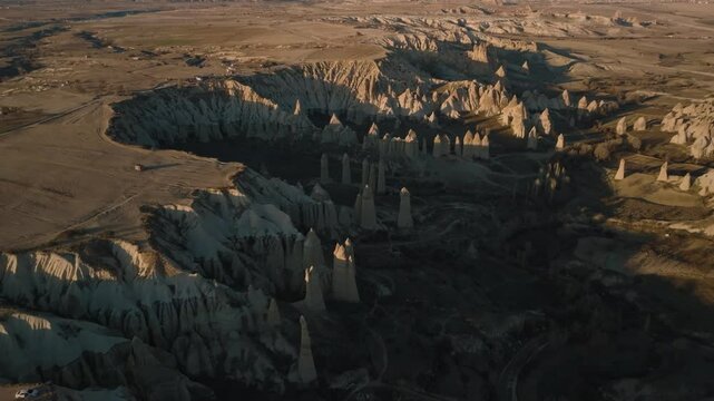Drone view from above at sunset of the elongated rocks in the Love Valley resembling chimneys or phalluses, with mountains in the background in Cappadocia