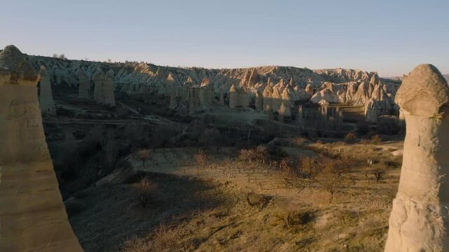 Drone flight between elongated unusual rock formations resembling chimneys or phalluses, illuminated by the sunset at the Love Valley in Cappadocia