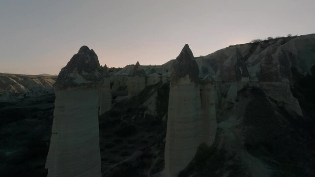 Drone flight between elongated unusual rock formations resembling chimneys or phalluses, illuminated by the sunset at the Love Valley in Cappadocia