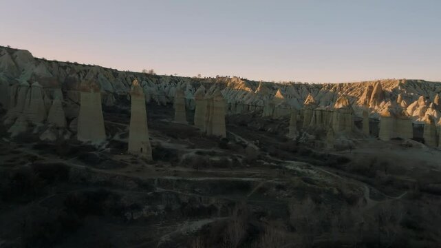 Drone flight between elongated unusual rock formations resembling chimneys or phalluses, illuminated by the sunset at the Love Valley in Cappadocia