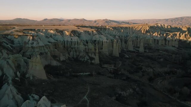 Drone flight between elongated unusual rock formations resembling chimneys or phalluses, illuminated by the sunset at the Love Valley in Cappadocia