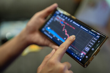 Action of a businessman is using mobilephone to review, chart analyse or trading during money or stock crisis loss situation. Financial tranding concept scene. Extreme close-up with soft focus.