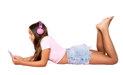 Little girl lying on the floor, using a smartphone and listening to the music. Side view. Full length studio shot isolated on transparent background.